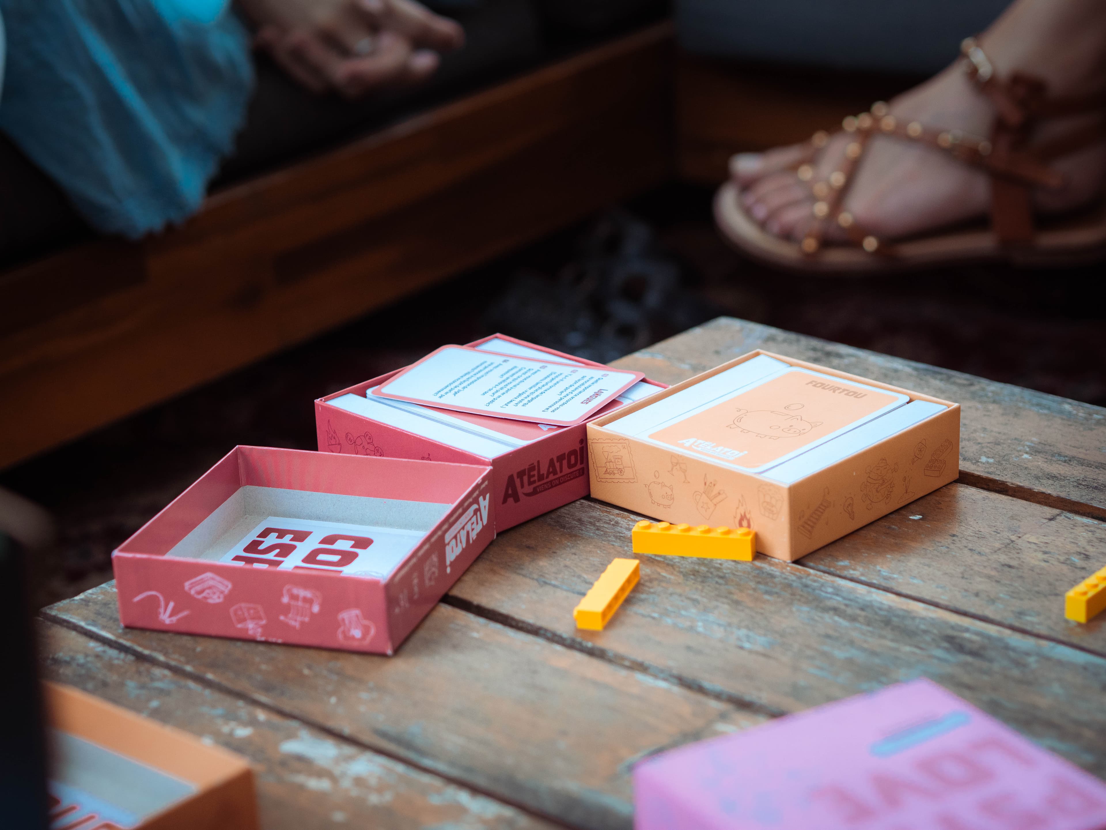 Les boîtes de jeux Atélatoi ouvertes, cartes étalées sur une table en bois